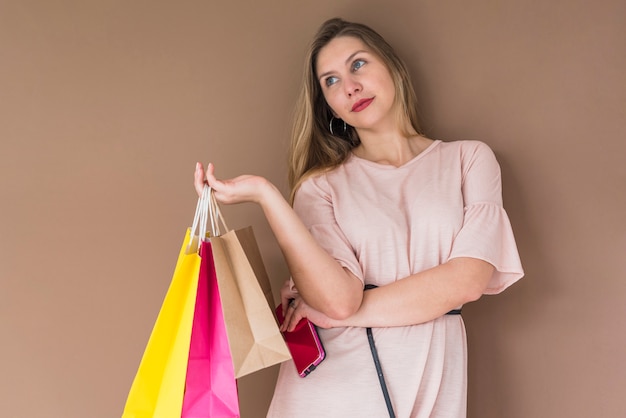 Photo gratuite jeune femme debout avec des sacs à provisions et smartphone