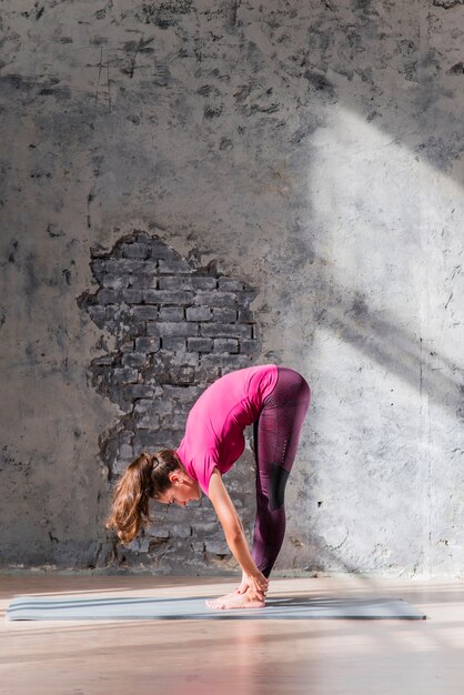Jeune femme debout sur un tapis d&#39;exercice faisant des exercices d&#39;étirement