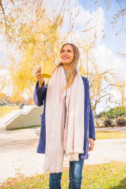 Jeune femme debout avec une tasse de thé dans le parc automne