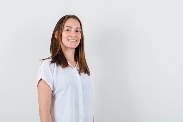 Jeune femme debout tout en souriant en chemisier blanc et à la recherche de confiance.