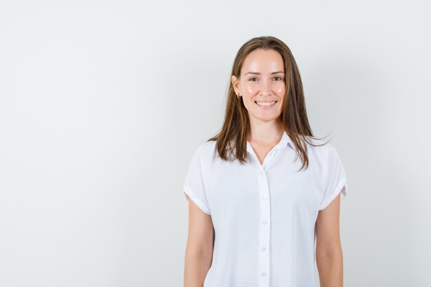 Jeune femme debout tout en souriant en chemisier blanc et à la recherche d'optimiste.