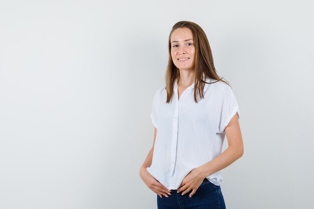 Jeune femme debout tout en souriant en chemisier blanc