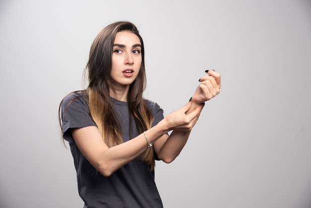 Jeune femme debout et vérifiant son pouls sur un fond gris.