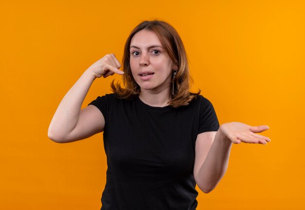 Jeune femme décontractée faisant le geste d'appel et montrant la main vide sur un mur orange isolé