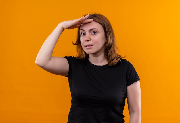 Jeune femme décontractée mettant la main sur le front et à la recherche sur le mur orange isolé