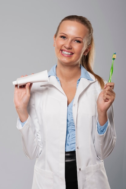 Jeune femme dentiste avec beau sourire tenant une brosse à dents et du dentifrice