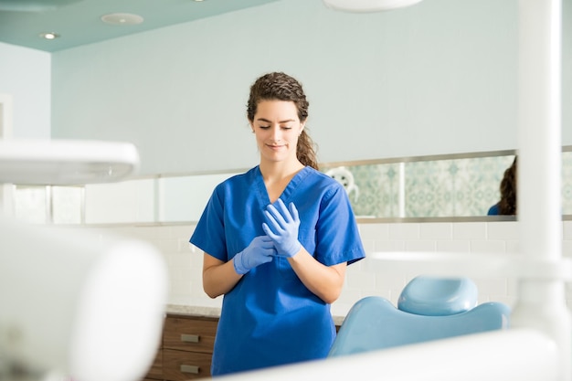 Jeune femme dentiste portant des gants chirurgicaux debout à la clinique dentaire