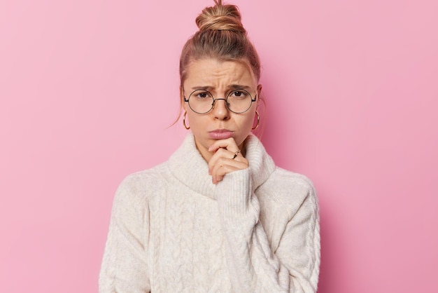 Une Jeune Femme Désespérée Et Malheureuse Regarde Avec Une Expression Insatisfaite Garde La Main Sur Le Menton Veut Pleurer Porte Des Lunettes Rondes Et Un Pull Blanc Décontracté Isolé Sur Fond Rose émotions Négatives