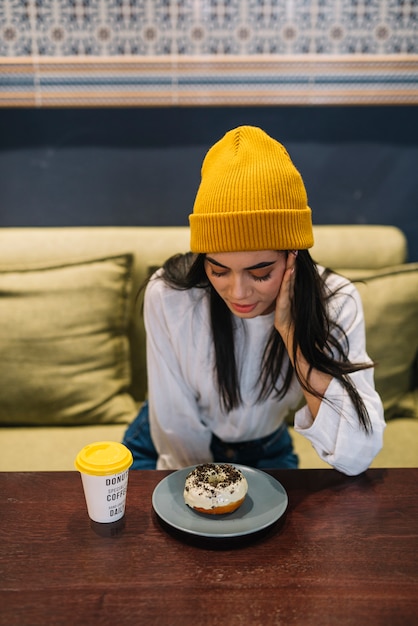 Jeune femme avec dessert sur une assiette près de tasse de boisson à table à café