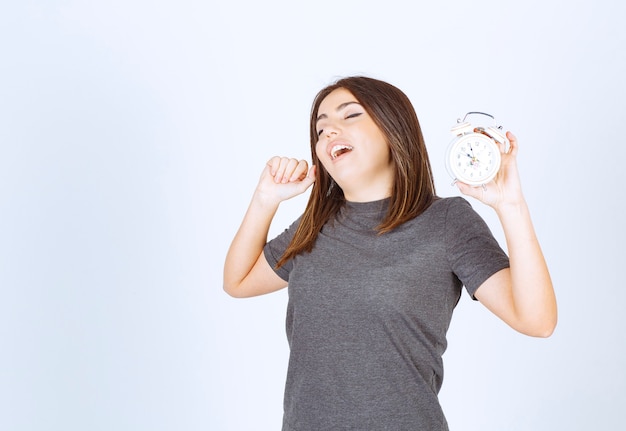 Photo gratuite jeune femme détendue en pyjama avec un réveil bâillant et debout.