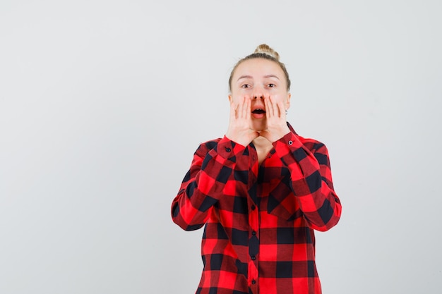 Jeune femme disant secret avec les mains près de la bouche en chemise à carreaux