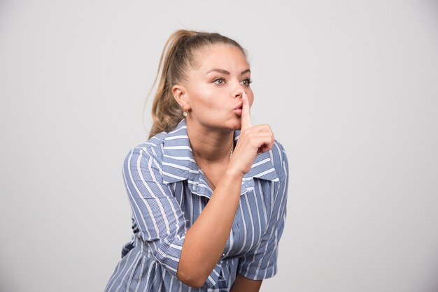 Jeune femme donnant un signe de silence sur un mur gris.