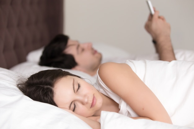 Photo gratuite jeune femme, dormir, tandis que, son, petit ami, utilisation, smartphone, dans lit