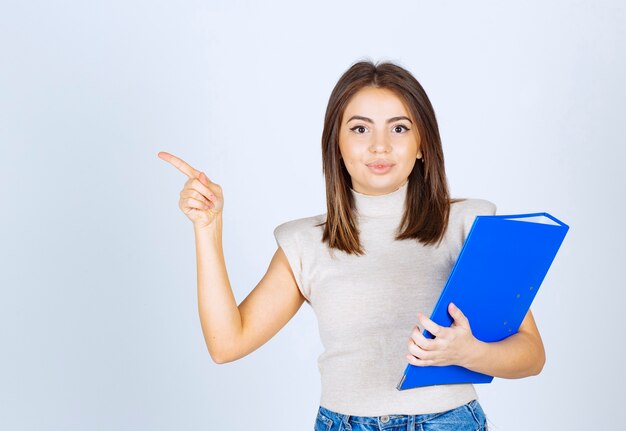 Jeune femme avec un dossier pointant vers l'extérieur avec un index.