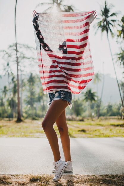 Jeune femme avec drapeau USA à rue tropicale