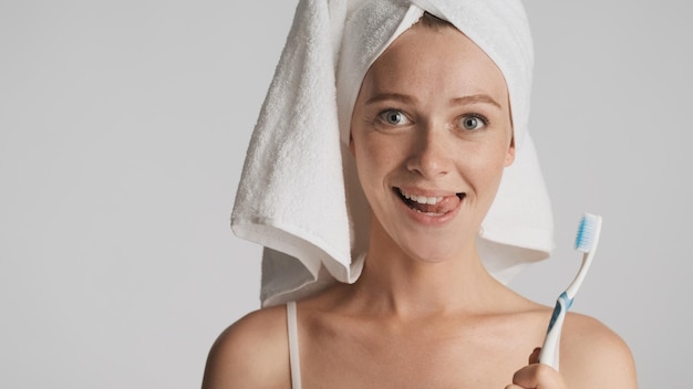 Jeune femme drôle avec une brosse à dents souriante montrant la langue à la caméra sur fond blanc