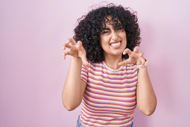 Jeune femme du moyen-orient debout sur fond rose souriant drôle faisant un geste de griffe comme chat expression agressive et sexy