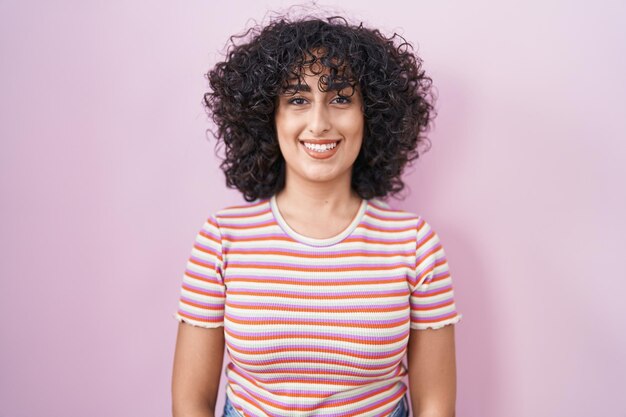 Jeune femme du Moyen-Orient debout sur fond rose avec un sourire heureux et cool sur le visage de la personne chanceuse