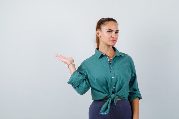 Jeune femme écartant la paume en chemise verte et semblant confiante. vue de face.