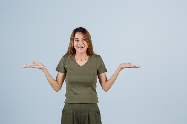 Jeune femme écartant les paumes en t-shirt, pantalon et ayant l'air heureuse, vue de face.