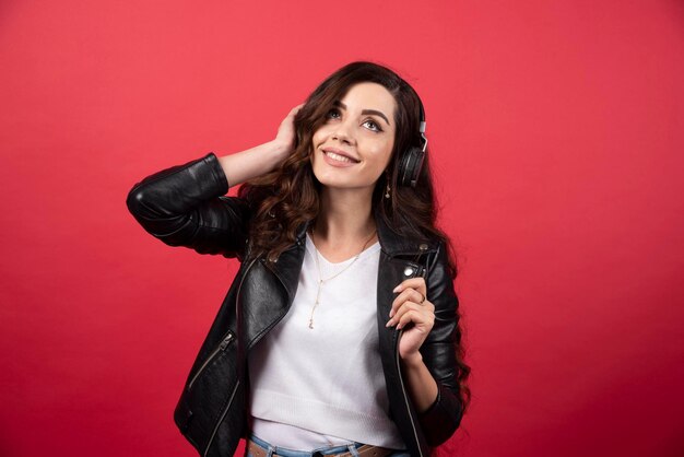 Jeune femme écoutant de la musique au casque et posant sur fond rouge. photo de haute qualité