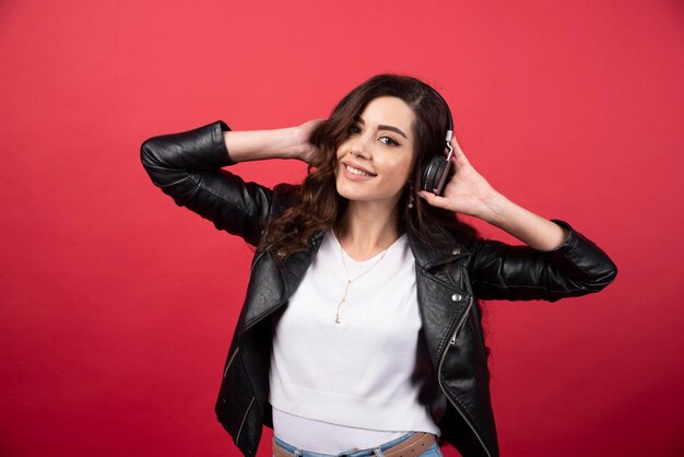 Jeune femme écoutant de la musique au casque et posant sur fond rouge. photo de haute qualité