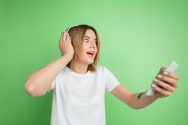 Jeune femme écoutant de la musique isolée sur le mur vert du studio