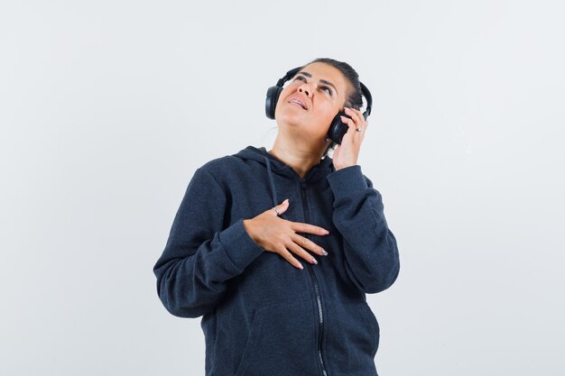 Jeune femme écoutant de la musique en veste et à la recherche concentrée. vue de face.