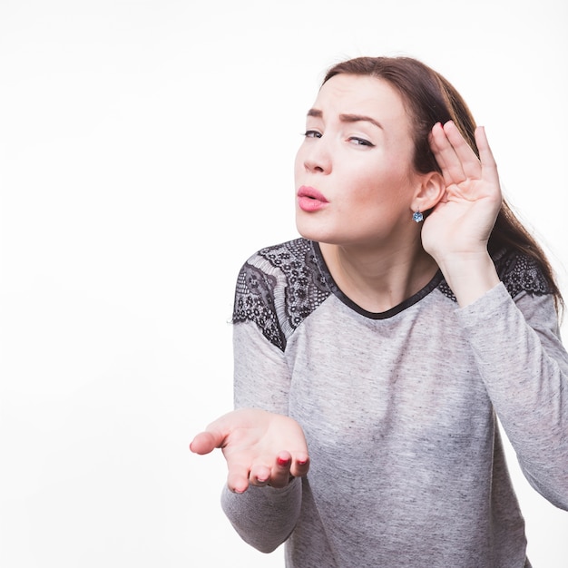 Photo gratuite jeune femme écoutant avec sa main sur une oreille sur fond blanc