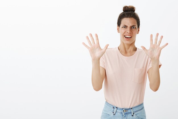 Jeune femme élégante inamusée et réticente posant contre le mur blanc