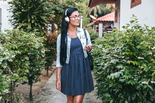 Jeune femme élégante marchant avec smartphone, écoutant de la musique au casque, vacances d'été