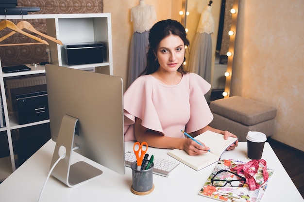 Jeune femme élégante en robe de luxe rose travaillant au bureau sur ordinateur