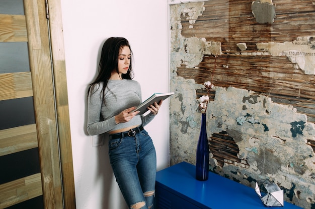 Photo gratuite une jeune femme élégante se penche sur le journal de lecture du mur