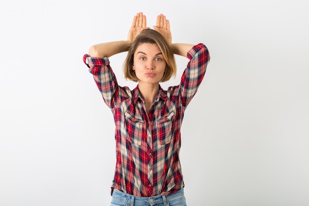 Jeune femme émotionnelle assez drôle en chemise à carreaux posant isolé sur un mur blanc de studio, montrant le geste de lapin