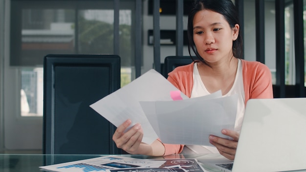 Photo gratuite jeune femme enceinte asiatique répertorie les revenus et les dépenses à la maison. maman fille heureuse en utilisant le budget d'enregistrement portable, taxe, document financier, commerce électronique travaillant dans le salon à la maison.