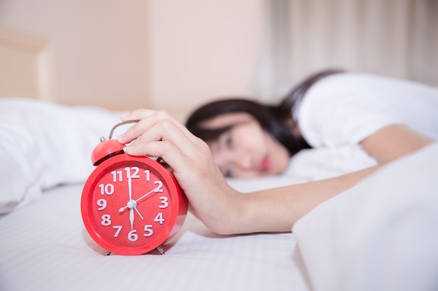 Jeune femme endormie et réveil dans la chambre à la maison