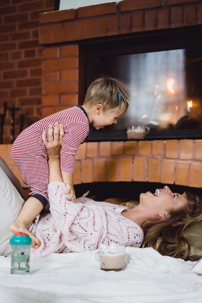 Jeune Femme Avec Un Enfant. Maman Et Son Fils S'amusent Autour De La Cheminée.