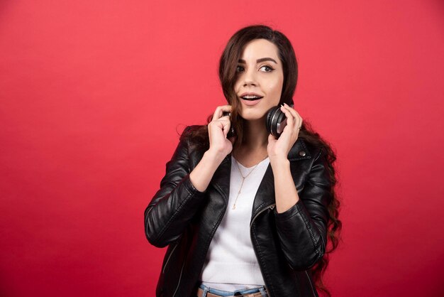 Jeune femme enlevant des écouteurs et posant sur un fond rouge. photo de haute qualité