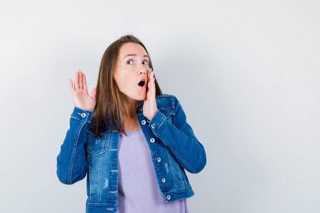 Jeune femme entendant une conversation privée en t-shirt, veste et semblant curieuse, vue de face.