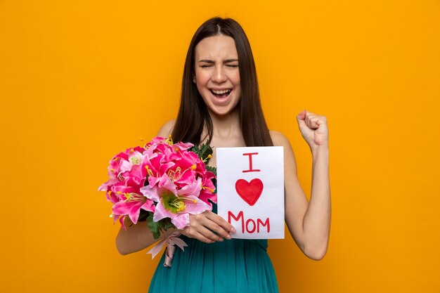 Jeune femme enthousiaste célébrant la fête des mères, tenant une carte de voeux et un bouquet