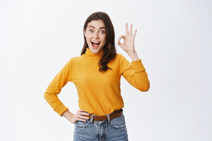 Photo gratuit jeune femme enthousiaste faisant la publicité d'un bon produit, montrant un signe ok et disant oui, approuvant quelque chose de cool, louant un choix génial, se tenant heureuse contre un mur blanc
