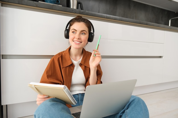 Une jeune femme enthousiaste a trouvé une solution et semble heureuse. Elle est assise par terre et fait ses devoirs sur son ordinateur portable.