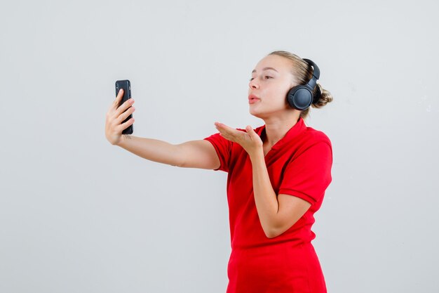 Jeune femme envoyant un baiser d'air sur appel vidéo en t-shirt rouge et écouteurs