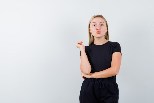 Jeune femme envoyant un baiser avec des lèvres boudeuses en t-shirt, pantalon et jolie. vue de face.