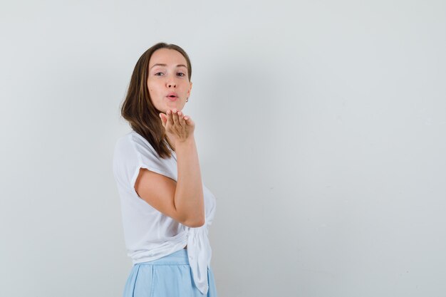 Jeune femme envoyant des bisous à l'avant en chemisier blanc et jupe bleu clair et à la charmante