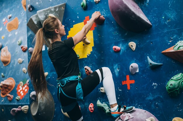 Jeune femme escaladant un grand mur d'escalade artificiel, à l'intérieur