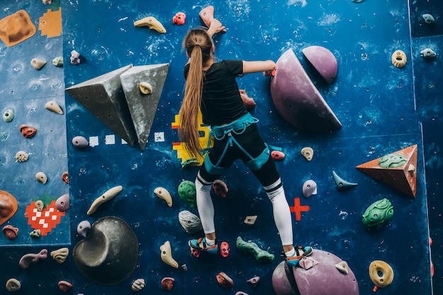 Jeune femme escalade un grand mur d'escalade artificiel, intérieur