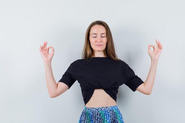 Jeune femme essayant de méditer en t-shirt noir et jupe bleue et à la détente