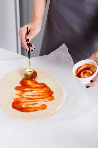 Jeune femme étalant la sauce tomate sur la pâte sur du papier sulfurisé