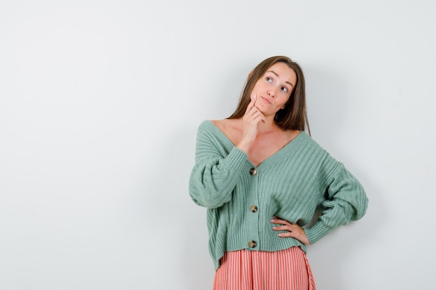 Jeune femme étayant le menton sur place en cardigan, jupe et à la rêveuse, vue de face.